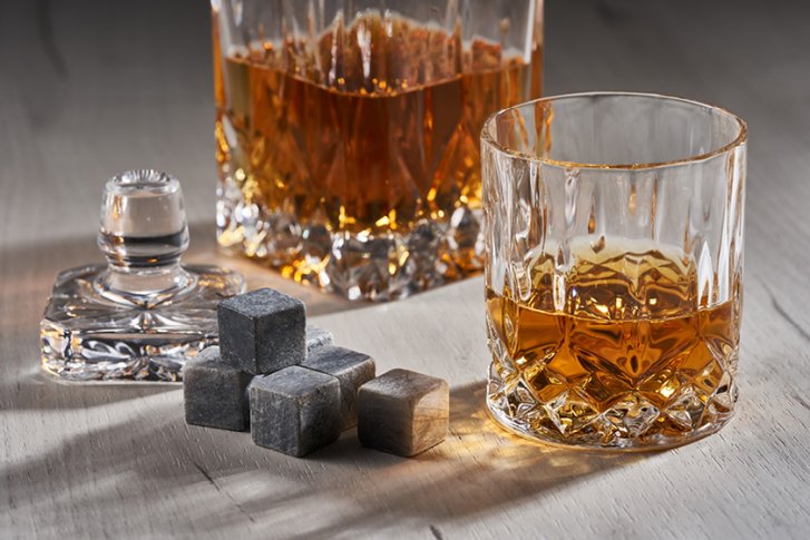 Karaffe und Glas mit Whisky stehen auf einem Tisch, umgeben von Kühlsteinen und Deckel.