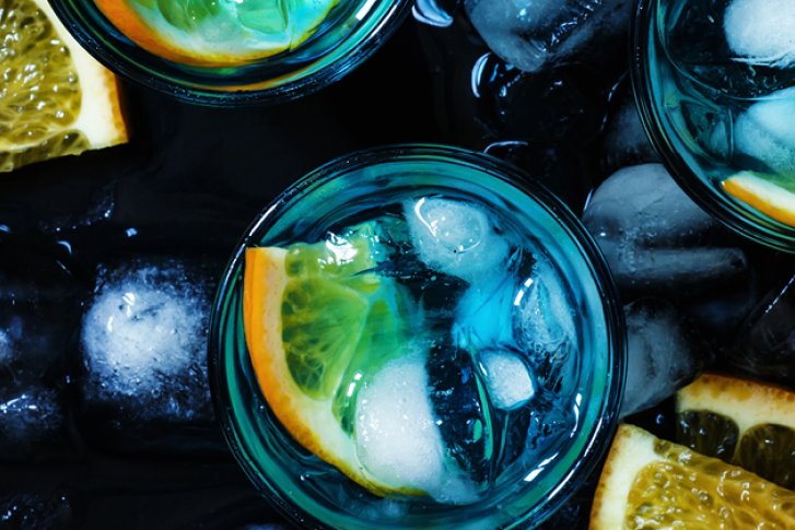 Drei Gläser mit Eis und Orangenscheiben stehen auf Eiswürfeln, umgeben von Zitronenscheiben.