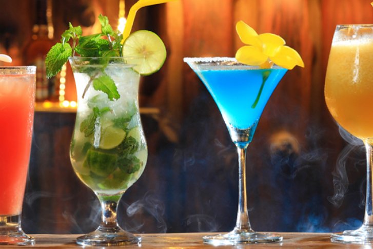 Verschiedene bunte Cocktails stehen auf einer Bar, dekoriert mit Früchten und Strohhalmen.