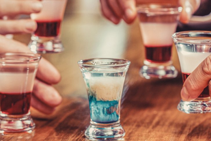 Gläser mit farbigen Schichten werden von Händen auf einem Holztisch gehalten und gehoben.