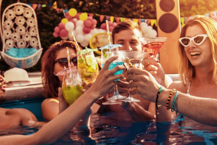 Personen stoßen mit Cocktails an, während sie in einem Pool feiern, umgeben von Dekoration.