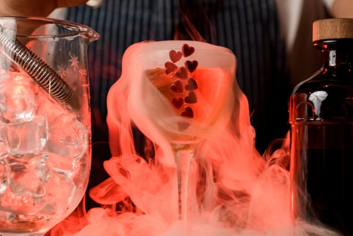 Glas mit Eiswürfeln, erzeugt Cocktails, vor rotem Licht und Rauch, neben einer Flasche.