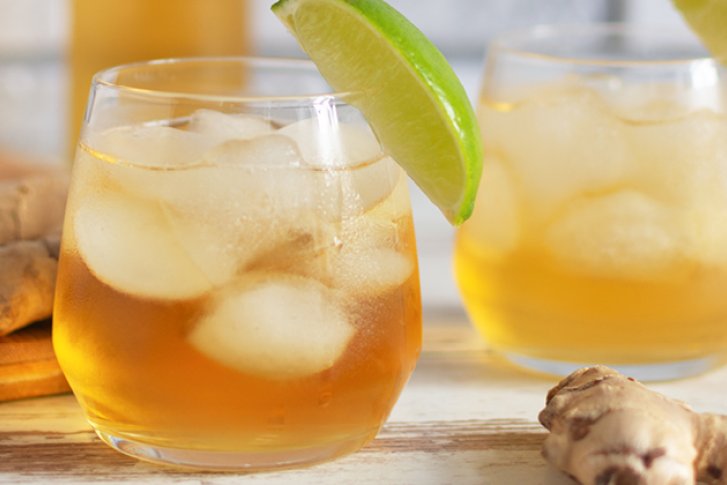 Zwei Gläser mit eisgekühltem Getränk, dekoriert mit Limetten, stehen auf Holztisch neben Ingwer.