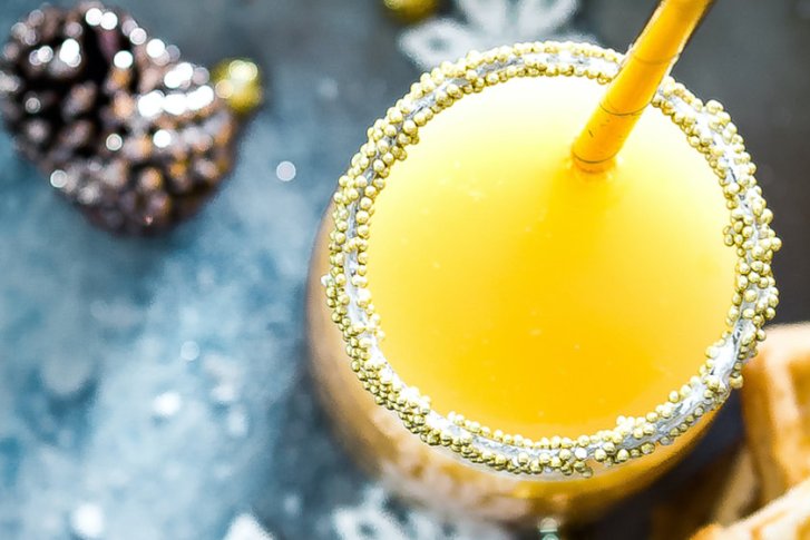 Gelbes Getränk mit Strohhalm steht dekorativ auf Tisch neben Waffeln und Tannenzapfen.