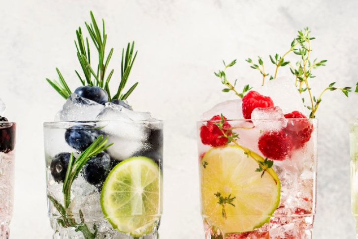 Vier bunte alkoholfreie Cocktails in Gläsern mit Eiswürfeln, frischen Früchten