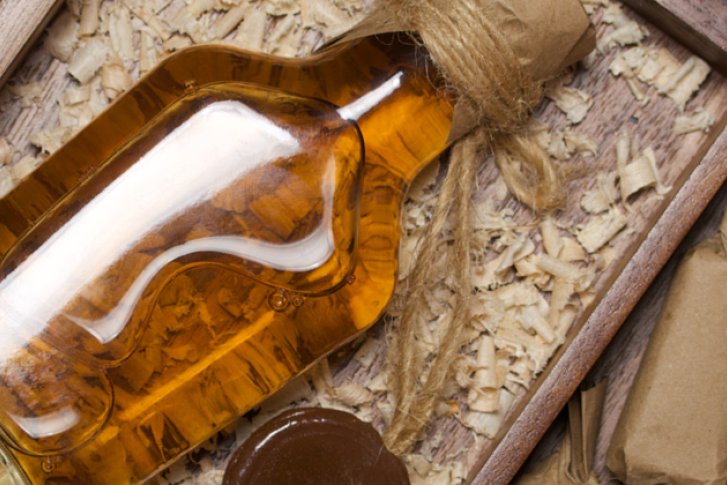 Eine Glasflasche liegt in einer Holzkiste, umgeben von Holzwolle auf Holzbrettern.