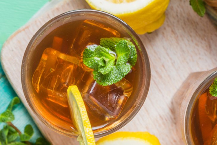 Zwei Gläser Eistee mit Minze und Zitronenscheiben auf Holzbrett, umgeben von Zitronen.