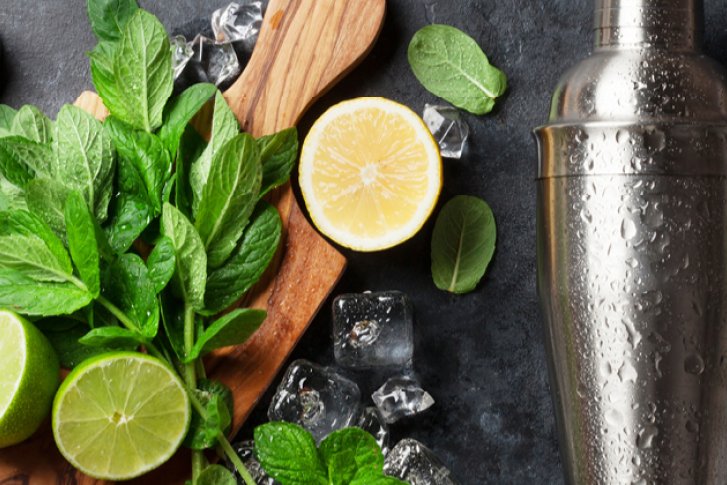 Küchenutensilien liegen neben frischen Limetten und Minze auf einem dunklen Tisch mit Eis.