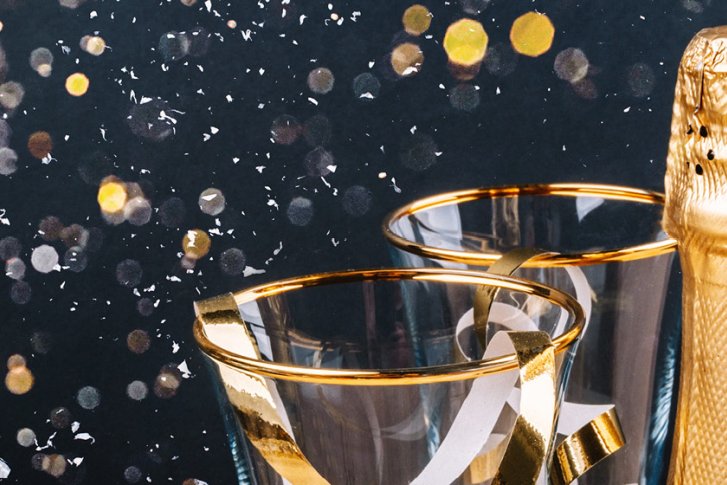 Zwei Sektgläser neben einer Champagnerflasche, goldener Glanz, vor dunklem, festlichem Hintergrund.