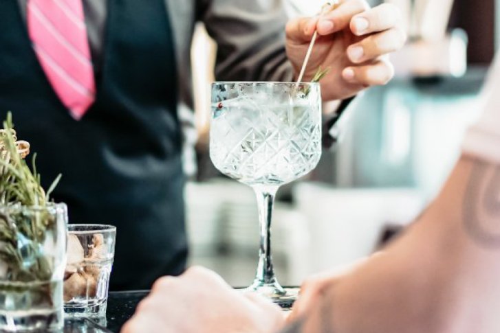 Barkeeper dekoriert Glas mit Kräuterzweig an einer Bar mit Getränkezubehör.