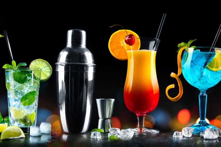 Verschiedene bunte Cocktails stehen nebeneinander, dekoriert mit Früchten und Eiswürfeln, auf schwarzem Hintergrund.