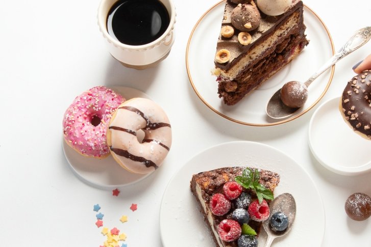 Donuts liegen auf einem Tisch, eine Hand hebt einen. Neben Kaffee und Kuchen.