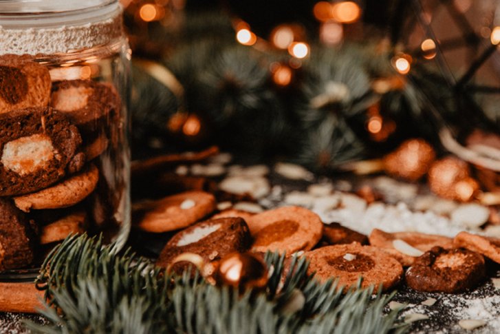Ein Glas voller Kekse steht in weihnachtlichem Ambiente mit Lichtern und Tannenzweigen.