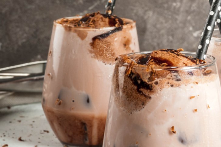 Drei Gläser mit Schokoladenmilch und Strohhalmen stehen auf einem Tisch, umgeben von Schokoladenstücken.