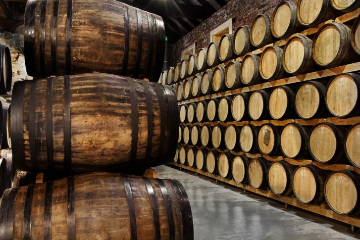 Holzfässer lagern gestapelt in einem rustikalen Weinkeller aus Backstein.