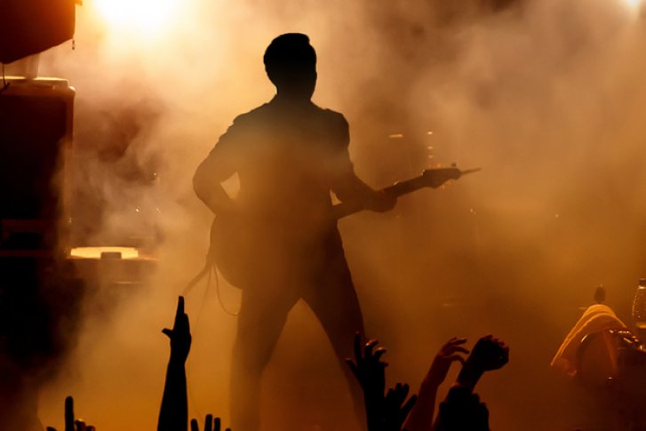 Gitarrist spielt auf der Bühne vor nebligem Hintergrund und jubelnden Händen im Publikum.