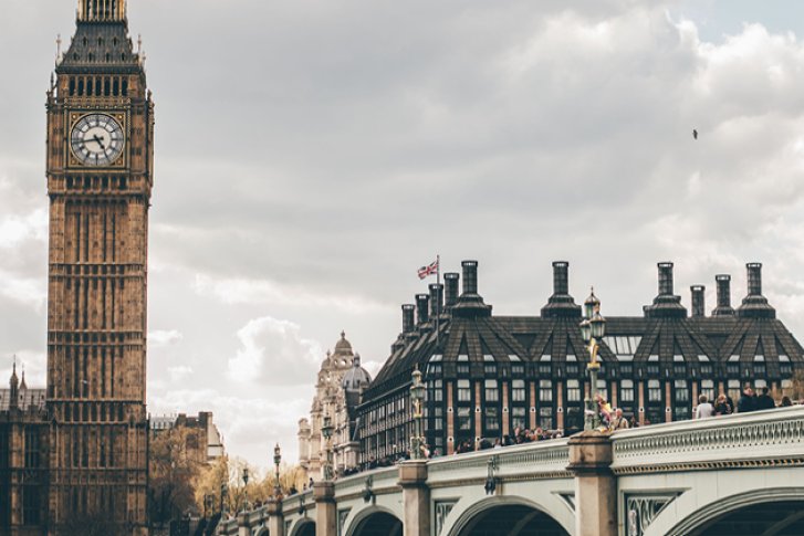 Großer Uhrturm zeigt Zeit, steht majestätisch vor bewölktem Himmel neben einer Brücke.