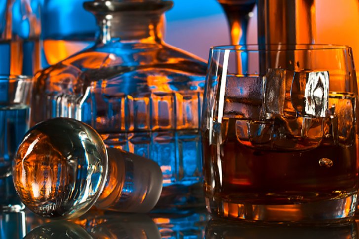 Gläser und Karaffe reflektieren buntes Licht, gefüllt mit Getränken und Eiswürfeln auf spiegelnder Oberfläche.