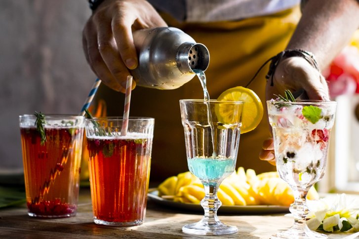 Cocktails werden von Hand aus einem Shaker eingeschenkt, auf einem Tisch mit Früchten.