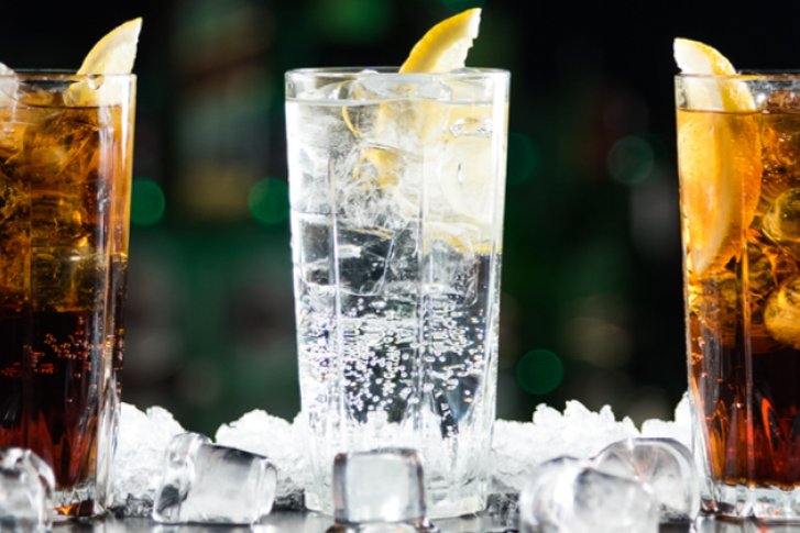 Drei Cocktailgläser mit Eiswürfeln und Zitronenscheiben stehen auf Eiswürfeln vor dunklem Hintergrund.