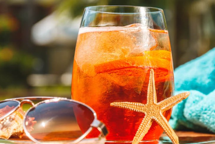 Ein Glas mit orangem Getränk steht neben einer Sonnenbrille auf einem Tisch im Freien.