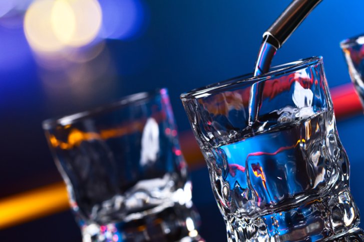 Gläser werden mit Flüssigkeit gefüllt, bunte Lichter im Hintergrund verleihen eine stimmungsvolle Atmosphäre.