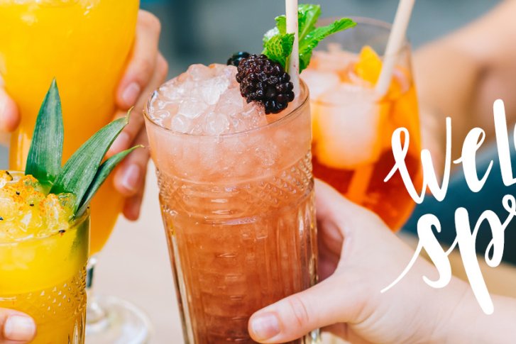 Cocktails stoßen an, feiern Frühling, leuchtende Farben, fröhliche Stimmung. Text: „Welcome Spring“.