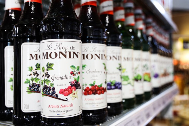 Flaschen mit Monin-Sirup stehen in einer Reihe im Verkaufsregal eines Ladens.