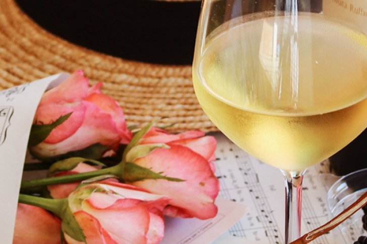 Weinglas steht auf einem Tisch mit Notenblatt, Blumen, Hut und Brombeeren.