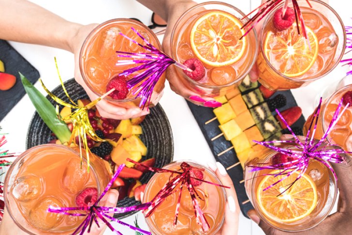 Cocktails werden mit Früchten dekoriert und in einer Gruppe von Menschen fröhlich angestoßen.