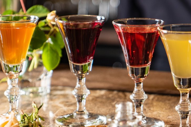 Verschiedenfarbige Cocktails stehen auf einer Theke, dekoriert mit Blumen und Minzblättern.