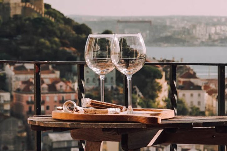 Zwei leere Weingläser stehen auf einem Holztisch mit Stadtaussicht im Hintergrund.