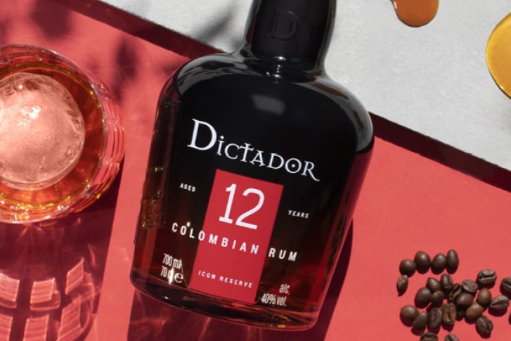 Eine Rumflasche liegt auf rotem Untergrund, daneben Glas, Kaffeebohnen und Flüssigkeitskreise.