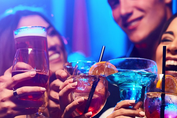 Menschen stoßen mit Cocktails in einer fröhlichen Feier in beleuchteter Partyumgebung an.