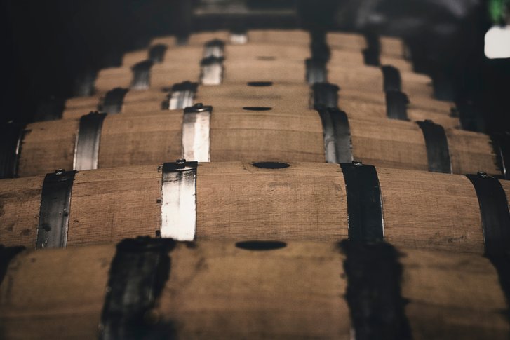 Holzfässer liegen aufgereiht in einem dunklen, lagerartigen Raum.