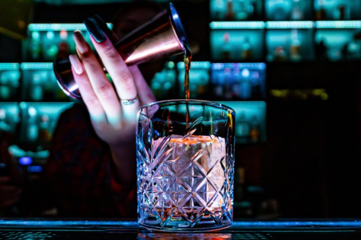 Glas wird gefüllt in einer Bar mit blauem Licht und Glasflaschen im Hintergrund.
