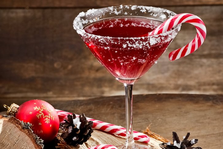 Rotes Cocktailglas mit Zuckerrand und Zuckerstange, dekoriert weihnachtlich auf Holzuntergrund.