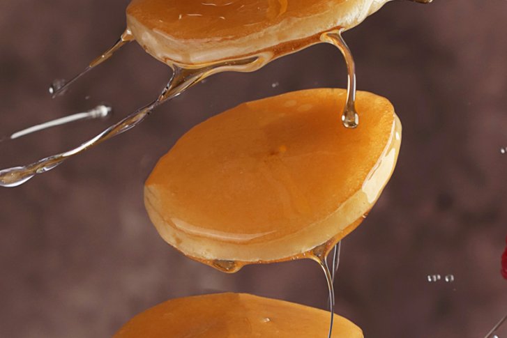 Pfannkuchen, von Honig bedeckt, schweben vor unscharfem Hintergrund, neben einer Himbeere.