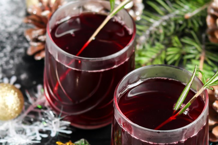 Zwei Gläser roten Getränks mit Rosmarin, umgeben von Tannenzweigen und weihnachtlichen Dekorationen.