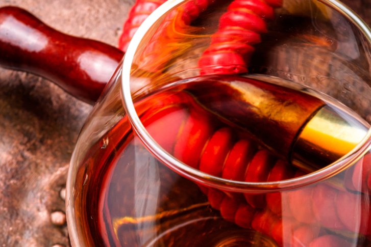 Ein Glas gefüllt mit braunem Getränk steht neben einem Holzgriff und roter Spirale.