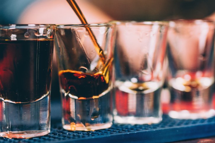 Gläser werden gefüllt, dunkles Getränk in Barumgebung. Hand im Hintergrund erkennbar.