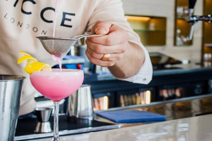 Rosa Cocktail wird durch ein Sieb gegossen, dekoriert mit Zitronenschale, in einer Bar.