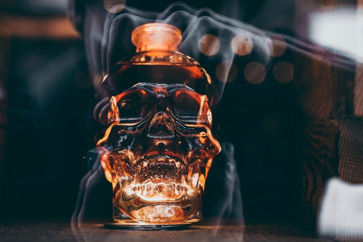 Eine Totenkopf-Flasche mit goldenem Getränk steht leuchtend und dekorativ auf einem dunklen Hintergrund.