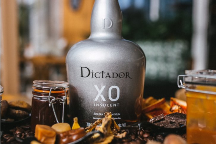 Eine silberne Rumflasche steht zwischen Gläsern mit Essigwaren auf einem Holztisch.