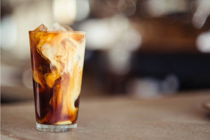 Ein Glas mit Kaffee und Sahne-Vermischung steht auf einer unscharfen, grauen Tischoberfläche.