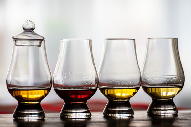 Vier Gläser mit farbigen Flüssigkeiten stehen auf einem Tisch vor unscharfem Hintergrund.