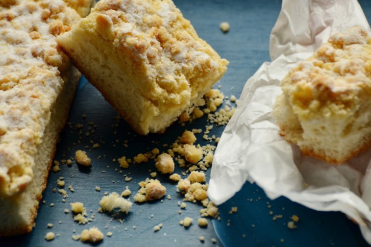 Kuchenstück – liegt aufgerissen – auf blauem Untergrund mit Krümeln und zerknittertem Papier.