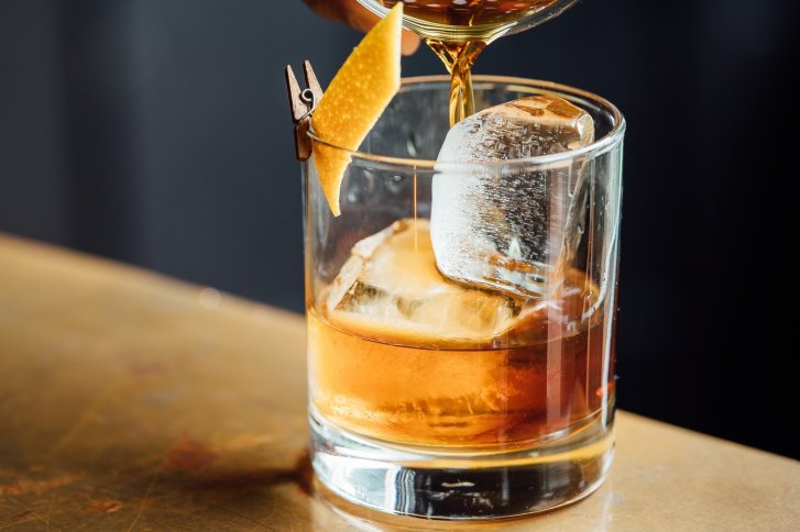 Ein Glas, gefüllt mit brauner Flüssigkeit und Eiswürfeln, auf einem hellen Tisch.