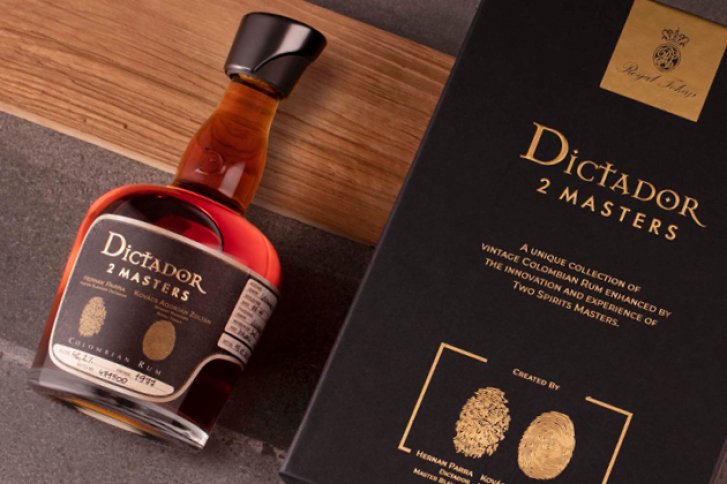 Eine Rumflasche liegt neben einer schwarzen Box auf hölzernem und steinigem Untergrund.