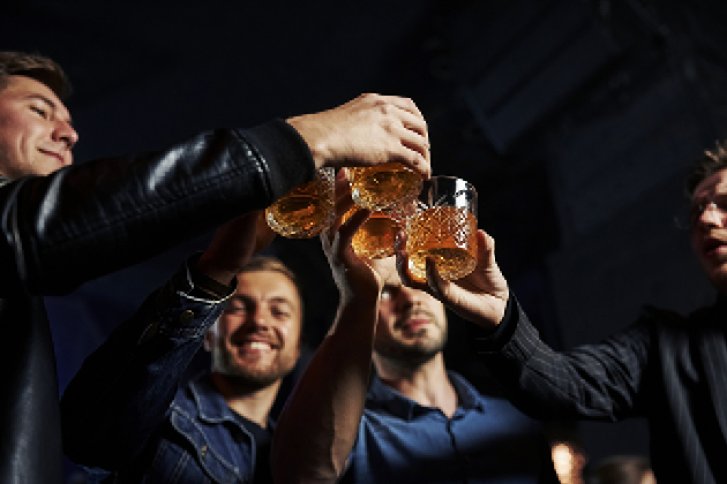 Personen stoßen mit Gläsern an in einer dunklen, fröhlichen Partyatmosphäre.